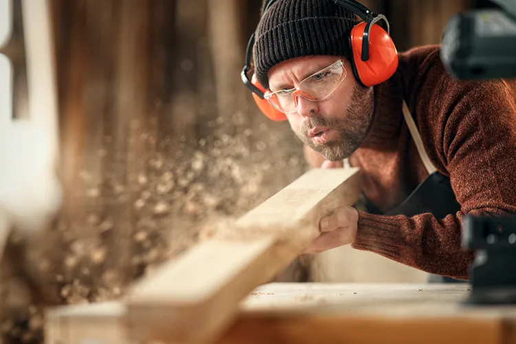 Erfahrener Schreiner arbeitet an Holzplatte in Werkstatt, Holzspäne fliegen – Fokus auf handwerkliche Präzision